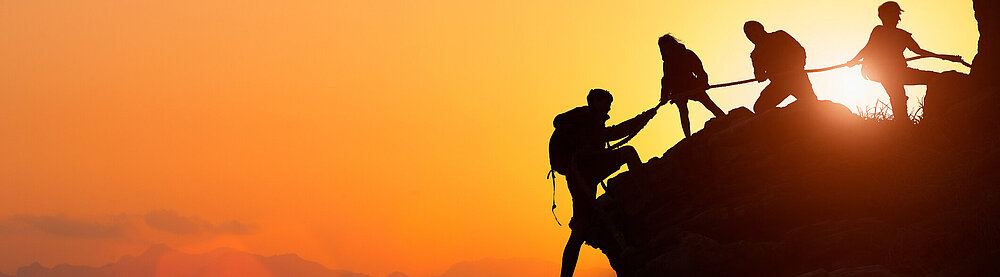 Silhouette des Kletterteams, das sich gegenseitig beim Klettern bei einem Sonnenuntergang hilft.
