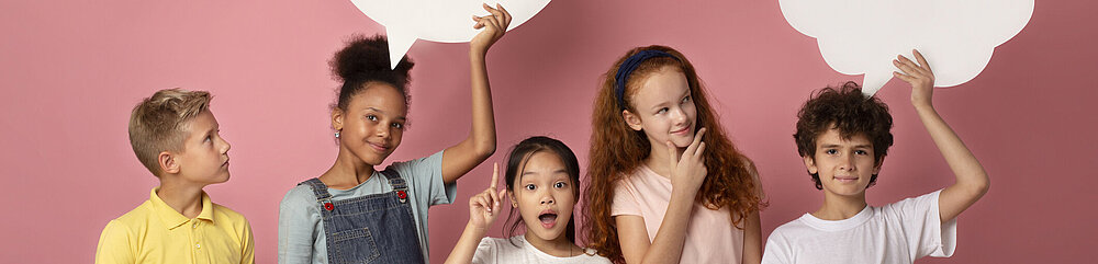 ©iStock\Prostock-Studio Nette multinationale Schulkinder mit leeren Sprechblasen über rosa Hintergrund, Raum für Design