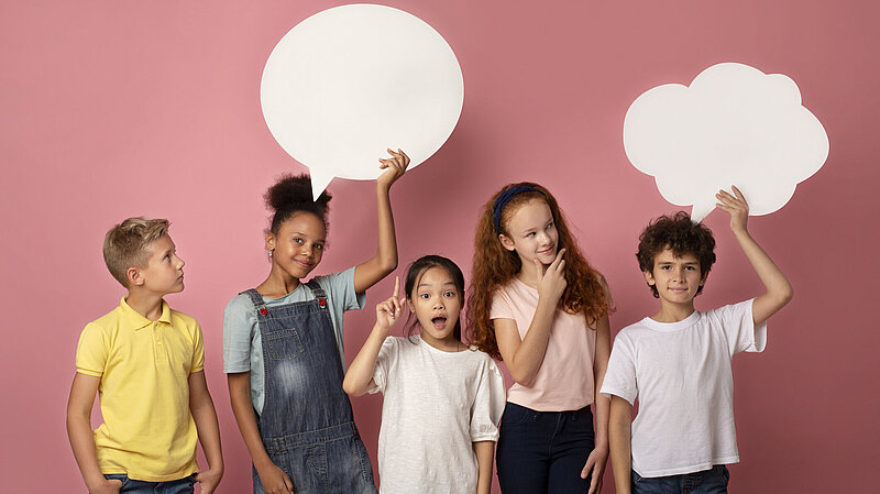 Nette multinationale Schulkinder mit leeren Sprechblasen über rosa Hintergrund, Raum für Design