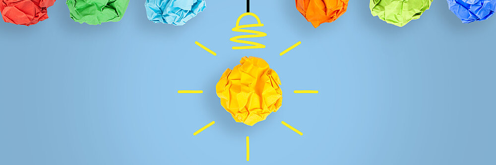 ©iStock\phototechno Auf dem Bild sind zerknüllte bunte Papierkugeln zu sehen, die wie Glühbirnen von der Decke hängen.