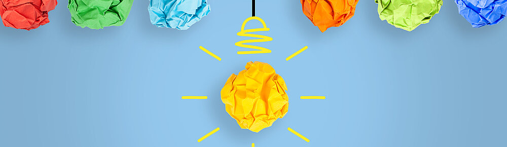 ©iStock\phototechno Auf dem Bild sind zerknüllte bunte Papierkugeln zu sehen, die wie Glühbirnen von der Decke hängen.