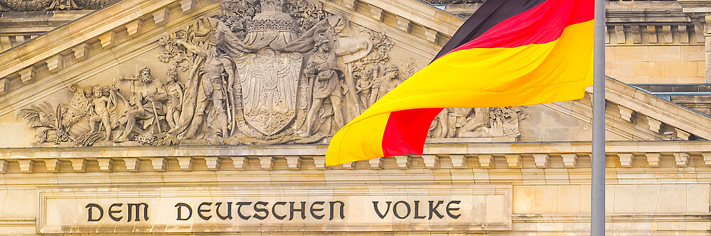 Deutsche Flagge auf einem Reichstagsgebäude im Hintergrund. Sitz des Deutschen Bundestages, Bezirk Berlin Mitte. Inschrift in deutscher Sprache: An das deutsche Volk