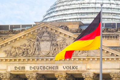 Deutsche Flagge auf einem Reichstagsgebäude im Hintergrund. Sitz des Deutschen Bundestages, Bezirk Berlin Mitte. Inschrift in deutscher Sprache: An das deutsche Volk