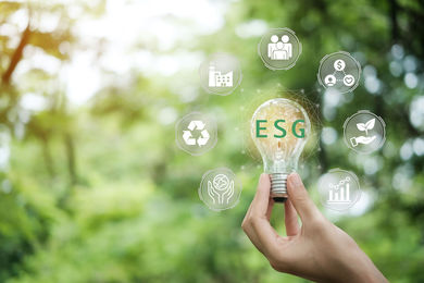 Handhaltende Glühbirne mit ESG-Icon-Konzept für Umwelt, Soziales und Governance im nachhaltigen und ethischen Wirtschaften auf der Netzwerkverbindung auf grünem Hintergrund.