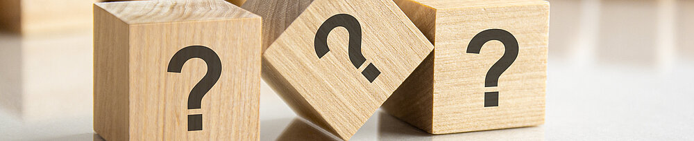 Drei Fragezeichen auf Holzwürfel geschrieben, auf dem grauen Tisch liegend, Konzept