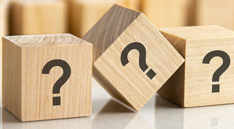 Drei Fragezeichen auf Holzwürfel geschrieben, auf dem grauen Tisch liegend, Konzept